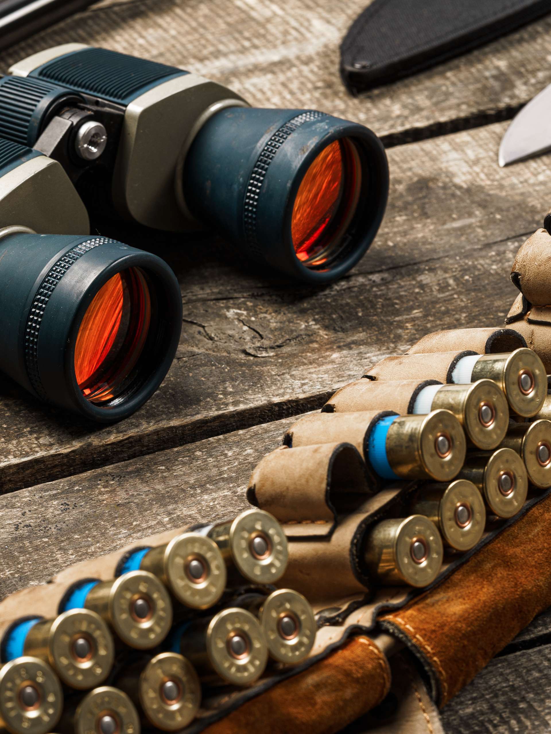 A collection of hunting gear including binoculars, a hunting knife, bullets, and noise canceling headphones.