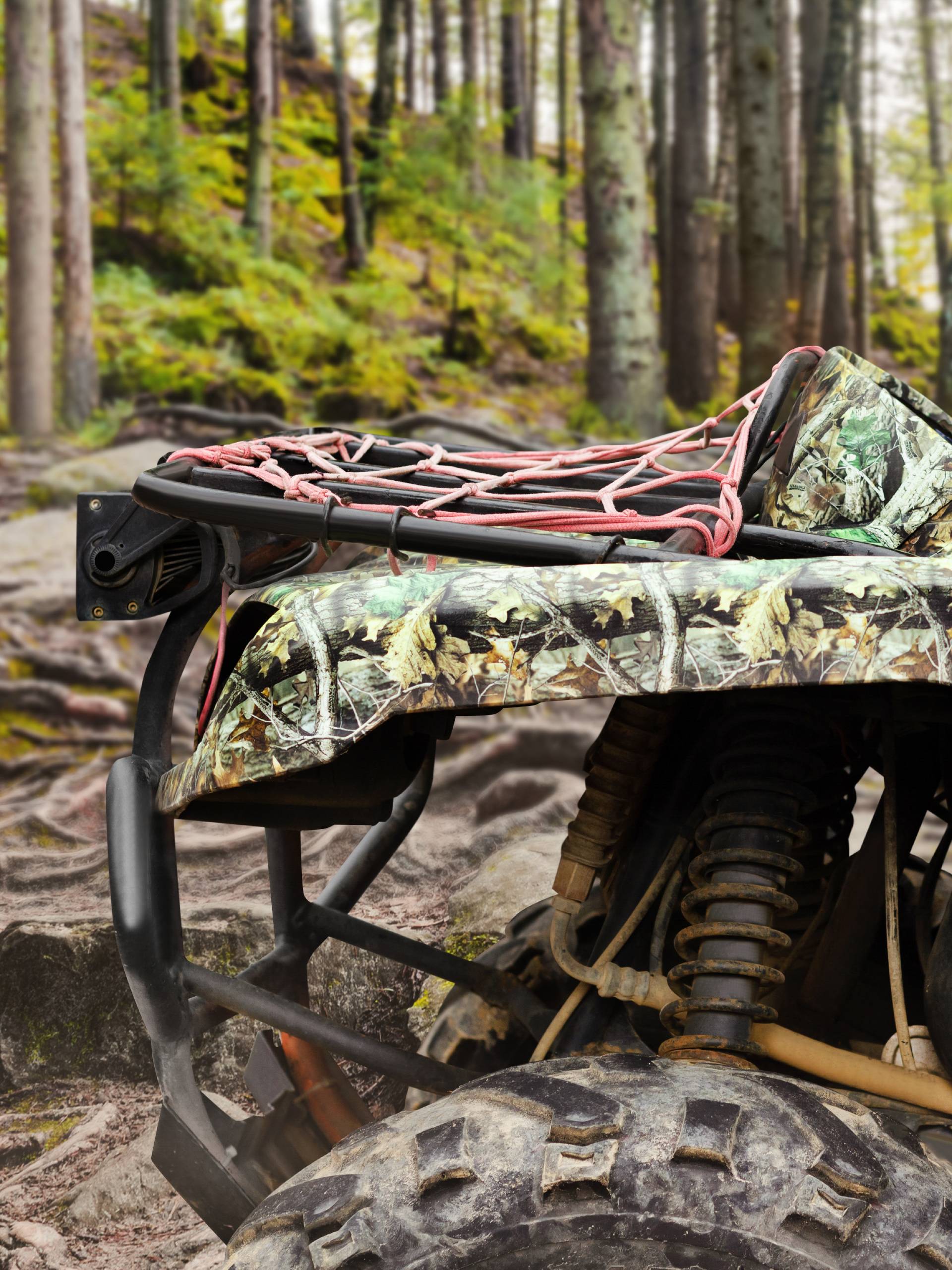 A camouflaged UTV is sitting in a forest, ready for a hunting trip. Several trees are in the background.