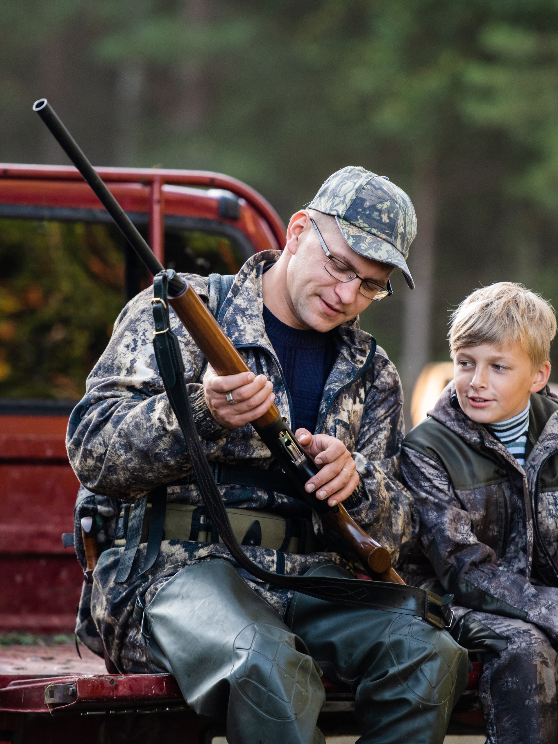 A father and son duo on a hunting trip. The father is showing the son the different parts of the rifle.