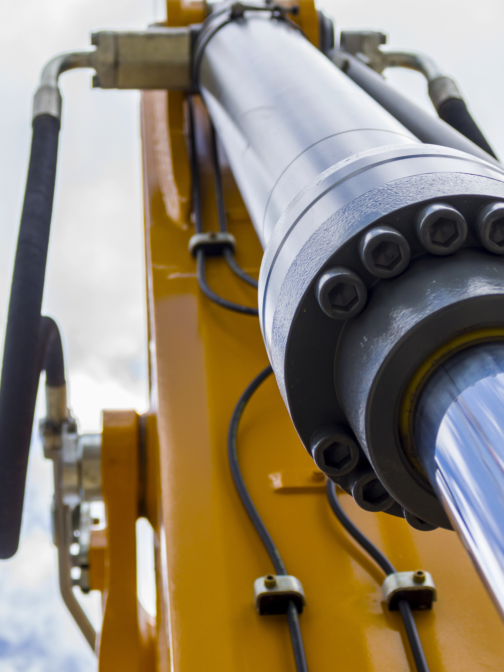 A silver hydraulic cylinder system connects to a yellow piece of heavy machinery. The blue sky is in the background.