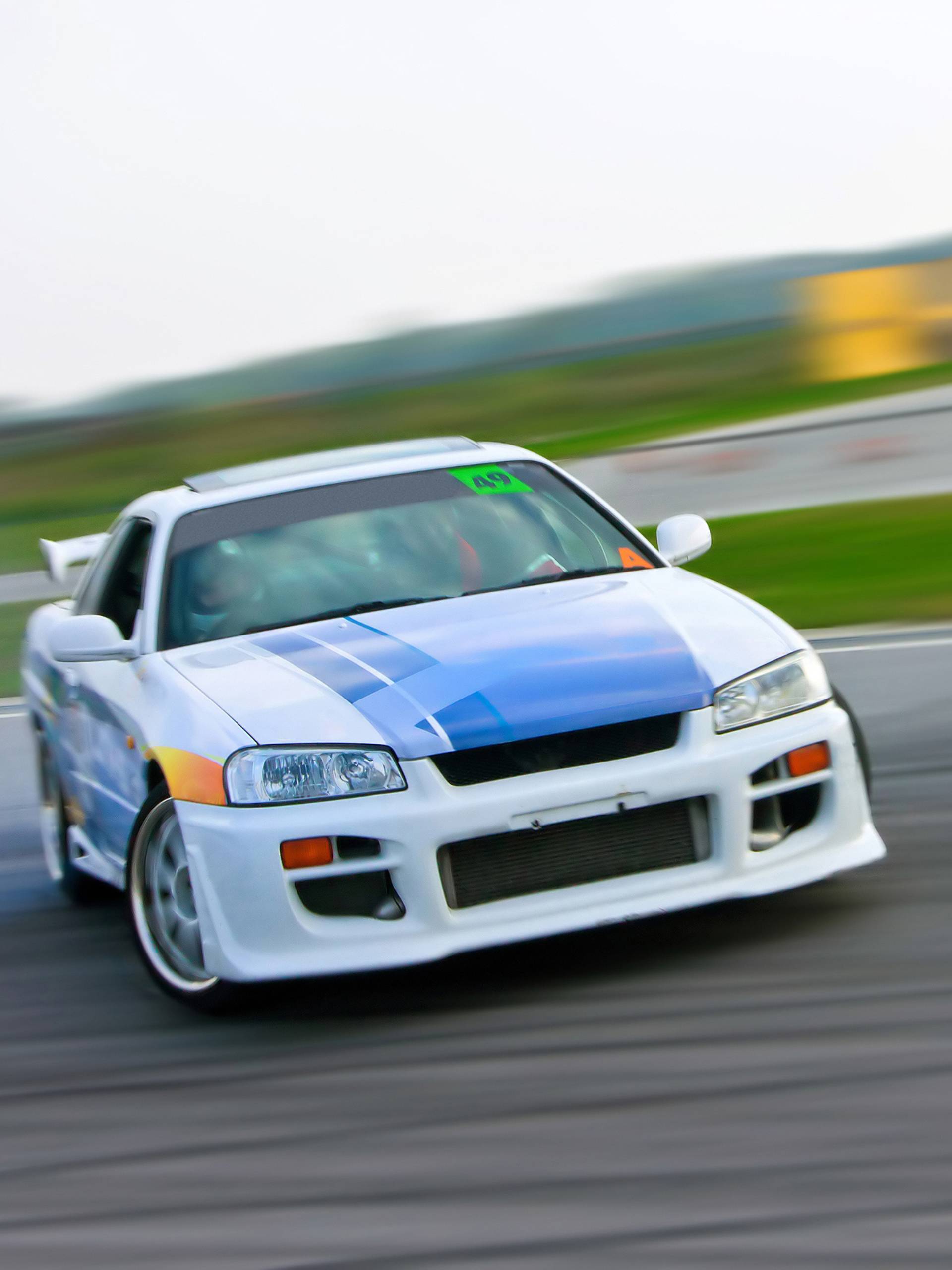 A white, blue, and orange race car skids down the race track. The background is blurry behind the car.