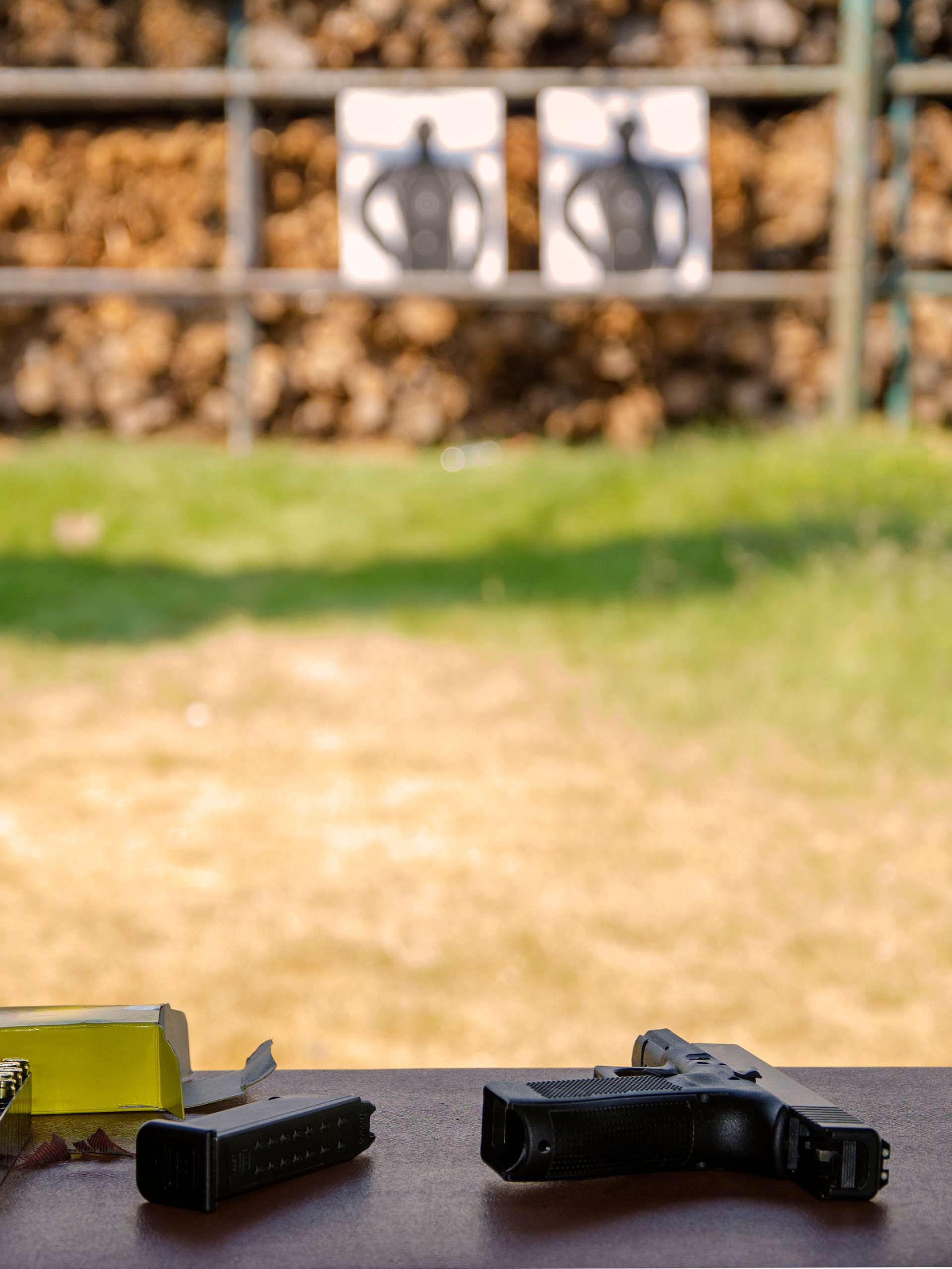 A shooting range with firearm and ammo sitting at range table across from targets and shooting range backstop.