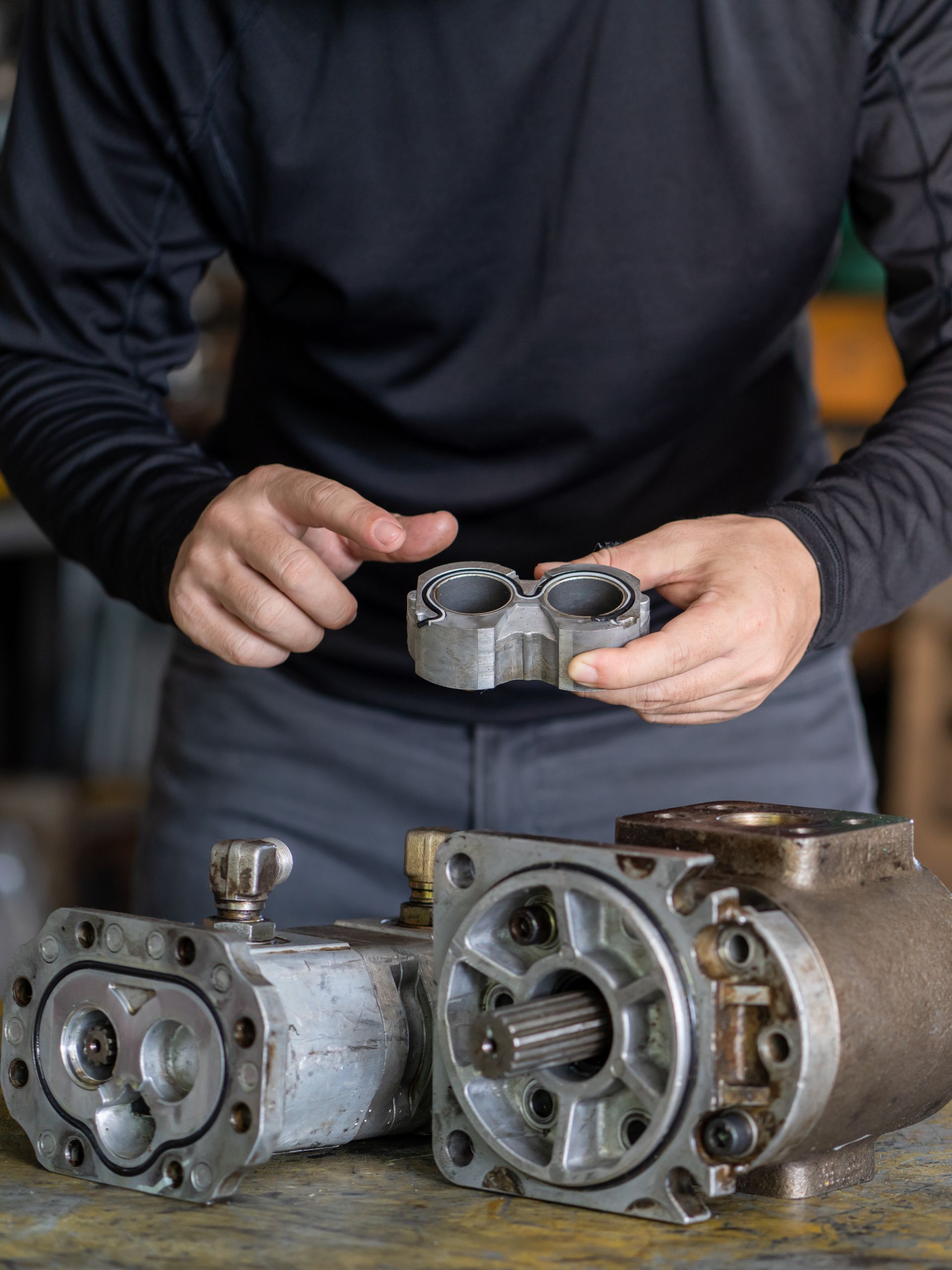 A person wearing black pants and a black shirt looks at a piece of machinery. They are holding one part of the machine. A person wearing black pants and a black shirt looks at a piece of machinery. They are holding one part of the machine.