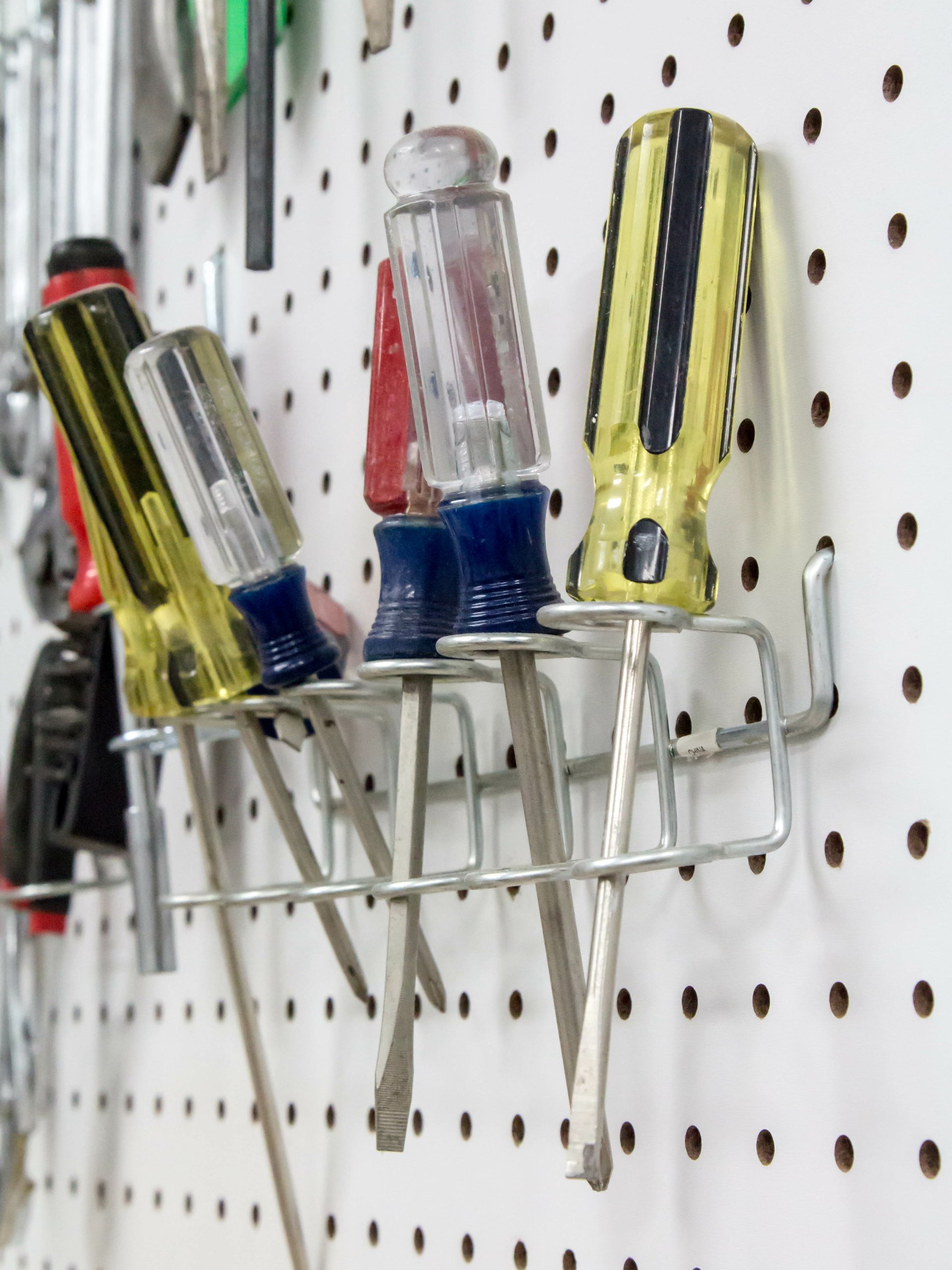 A close-up view shows Phillip's head and flat-head screwdrivers of various lengths hanging on a white pegboard.