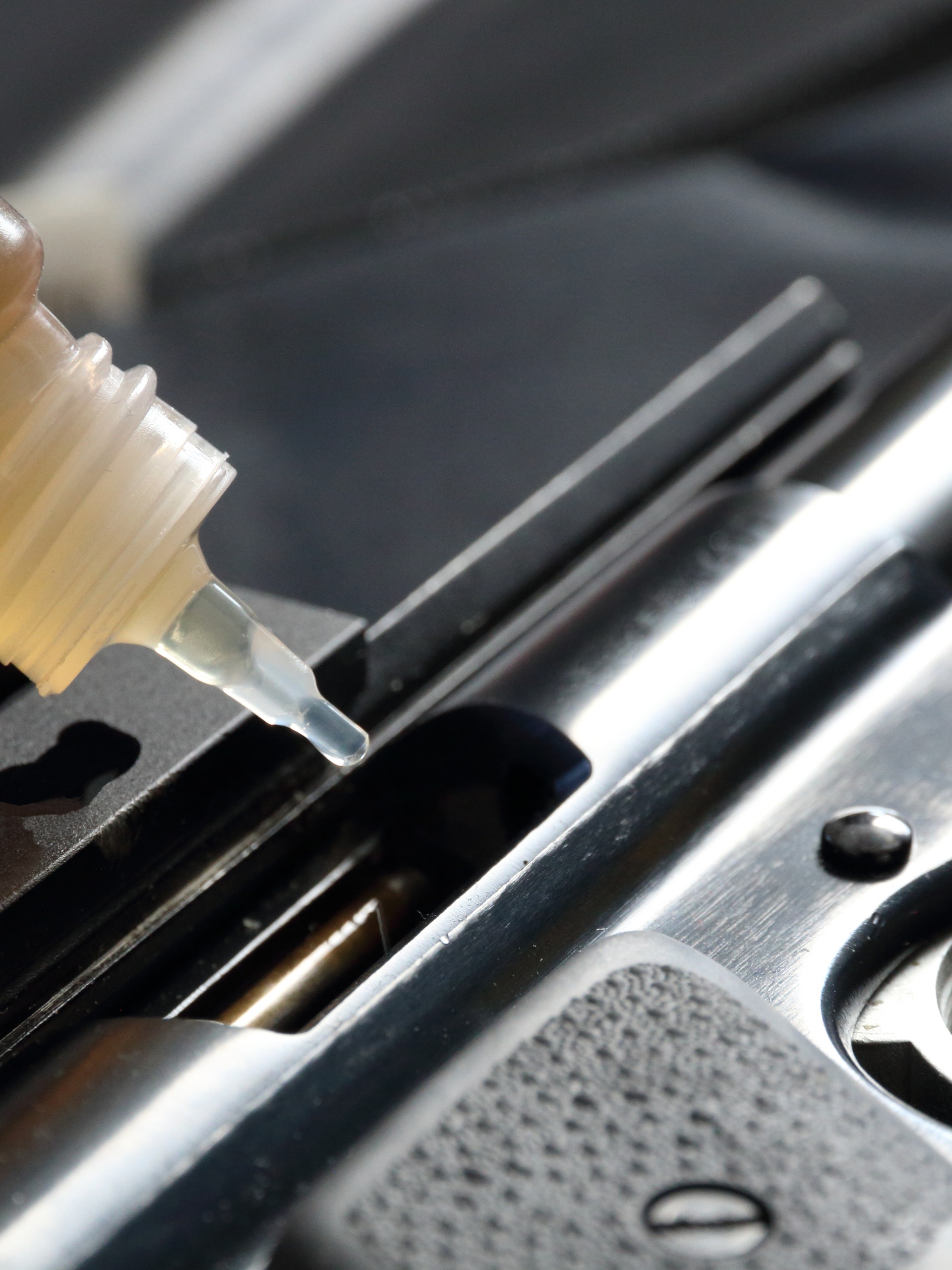 A close-up of a clear bottle labeled "lubricant" being used to oil a firearm resting on a table covered with black cloth.