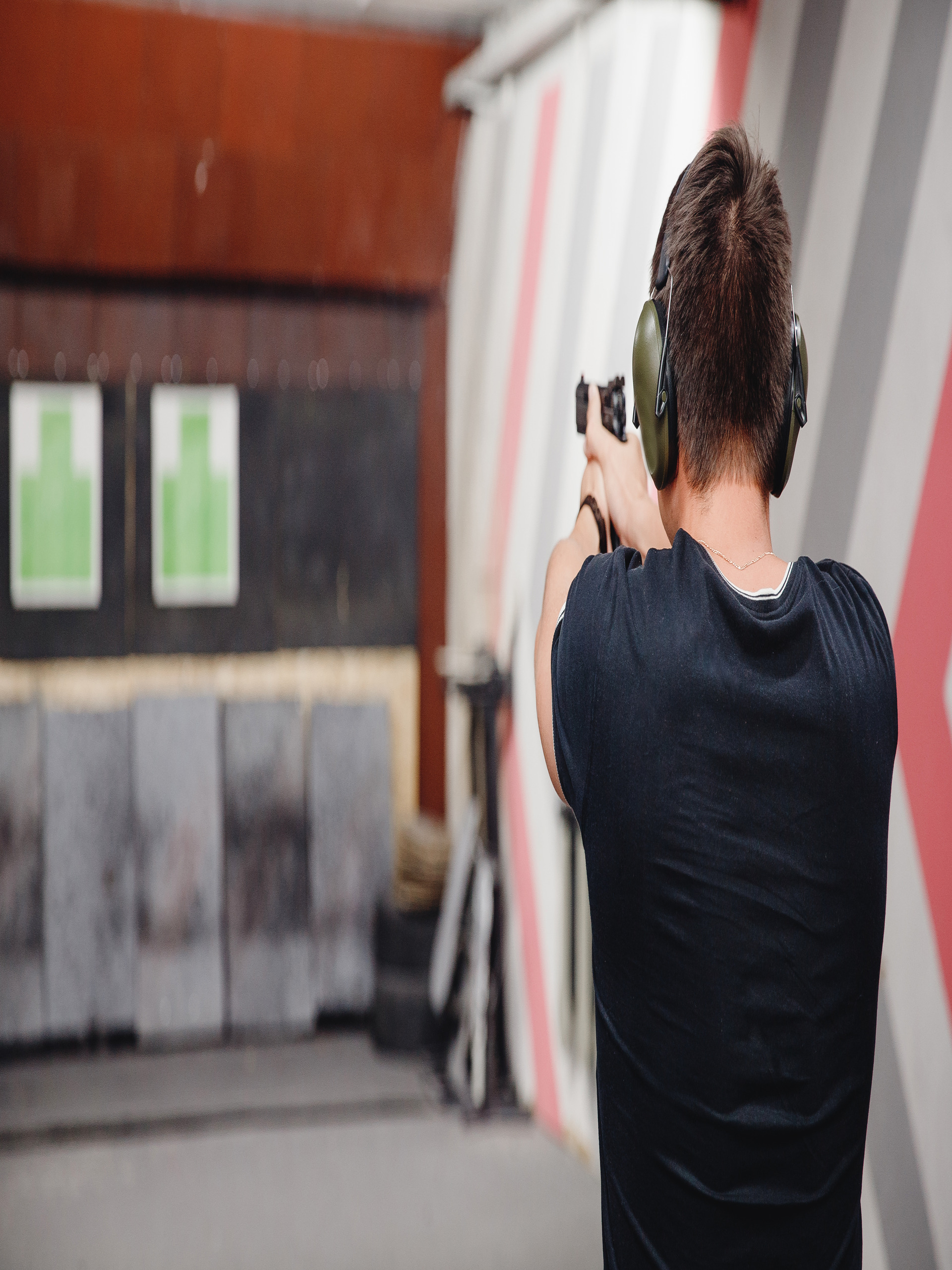 A person in a black T-shirt and protective ear coverings holding a pistol and preparing to fire in an indoor range.