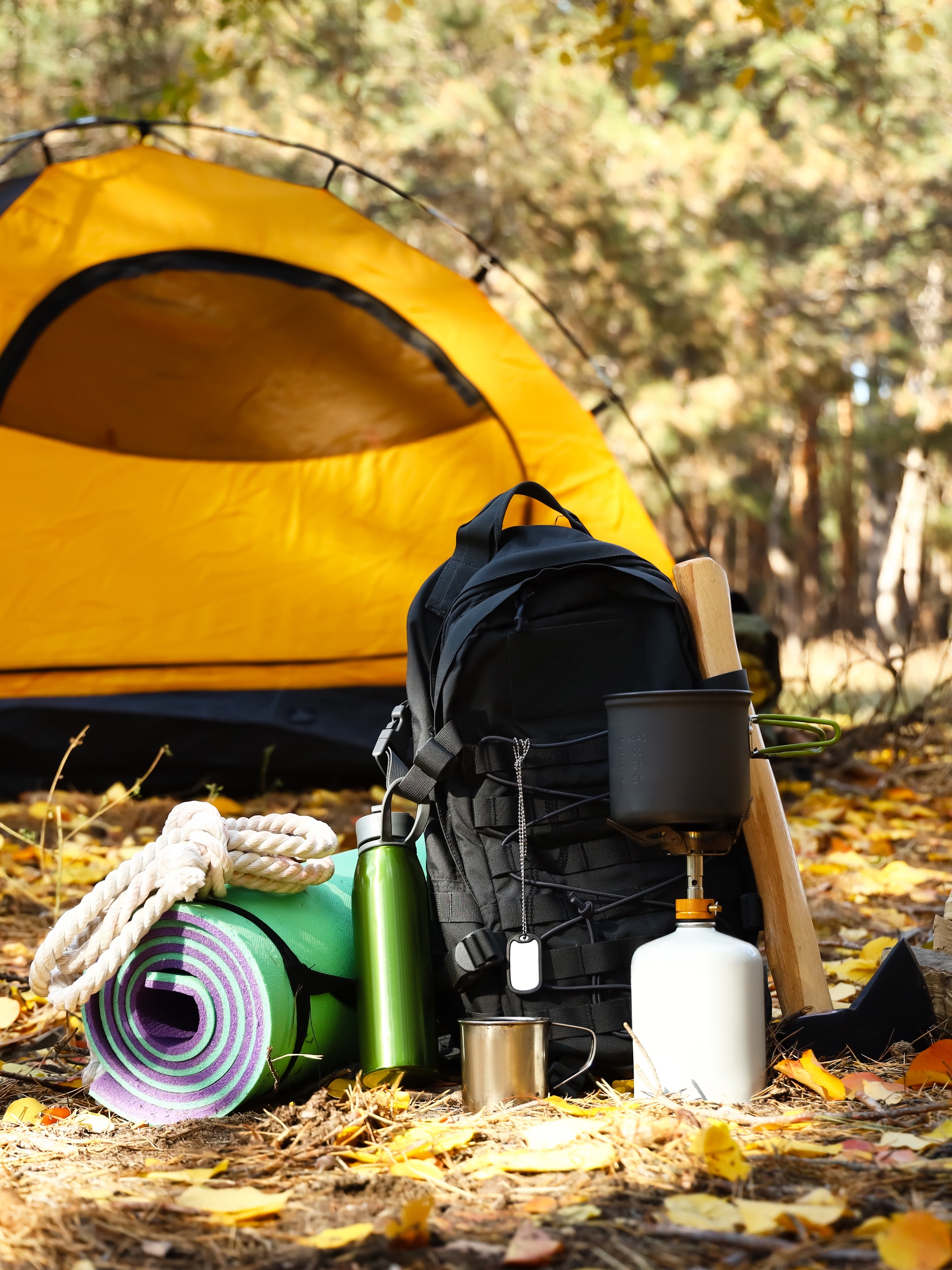 A yellow tent for camping sitting in a forest during the fall with a pile of gear sitting in front of it during the day.